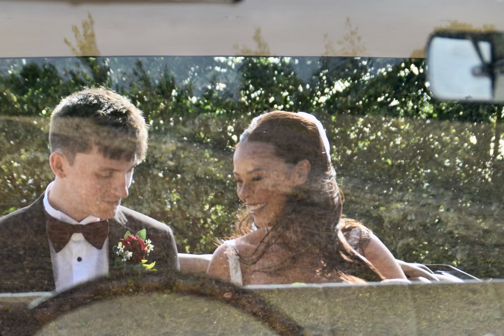A bride and groom sharing a tender moment in a car, with greenery visible in the background.