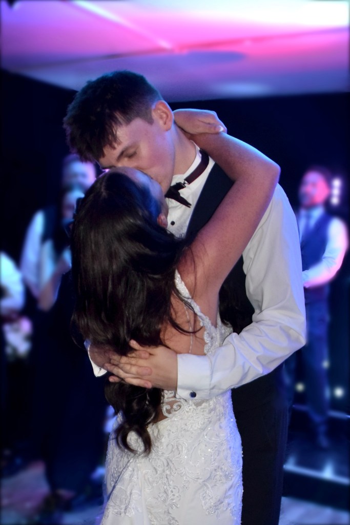 A couple sharing a romantic kiss during their first dance at a wedding, surrounded by softly lit decorations.
